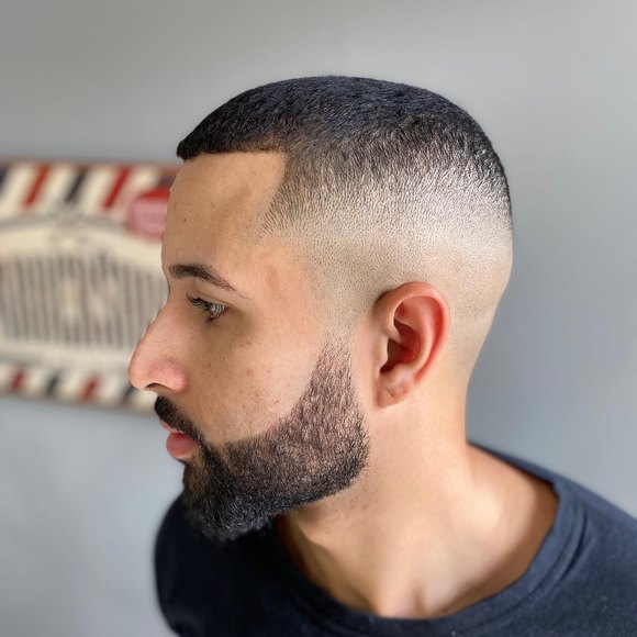 Corte baixo com barba cheia alinhada, de perfil.