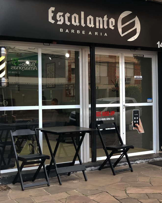 Fachada da Escalante Barbearia, com o letreiro sobre a porta de vidro e as mesinhas na calçada.