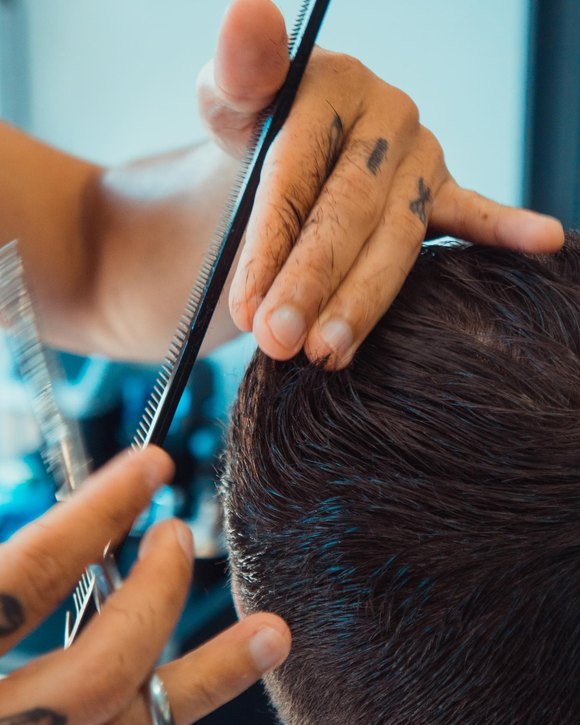 Tesoura e pente trabalhando o topo do cabelo, mão do barbeiro em primeiro plano.
