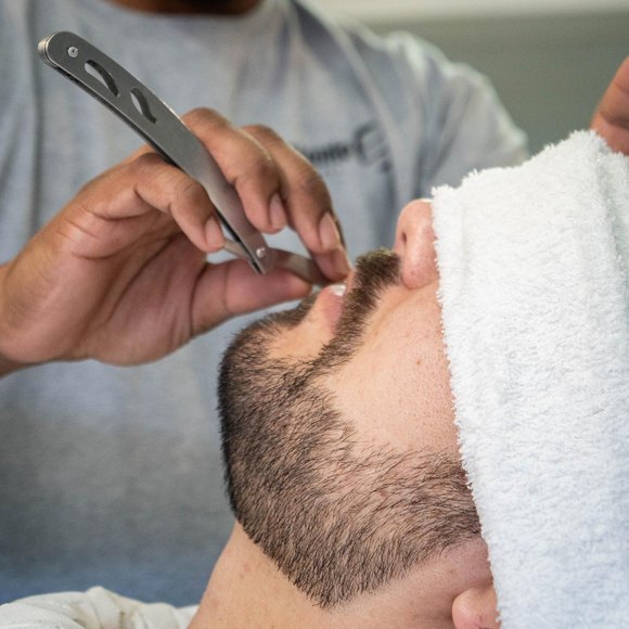 Acabamento da barba com navalha, toalha quente enrolada na testa do cliente.